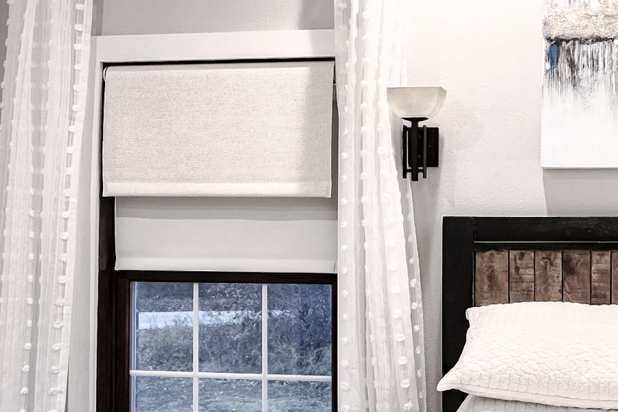 Don't want to get out of bed to fix the window shades? You don't have to with motorized shades! White motorized roller shade on a bedroom window