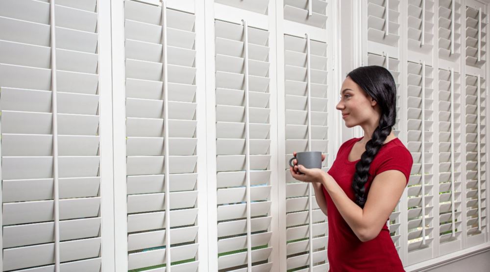 Plantation shutters can be custom fit to any specialty type window. Woman admiring plantation shutters