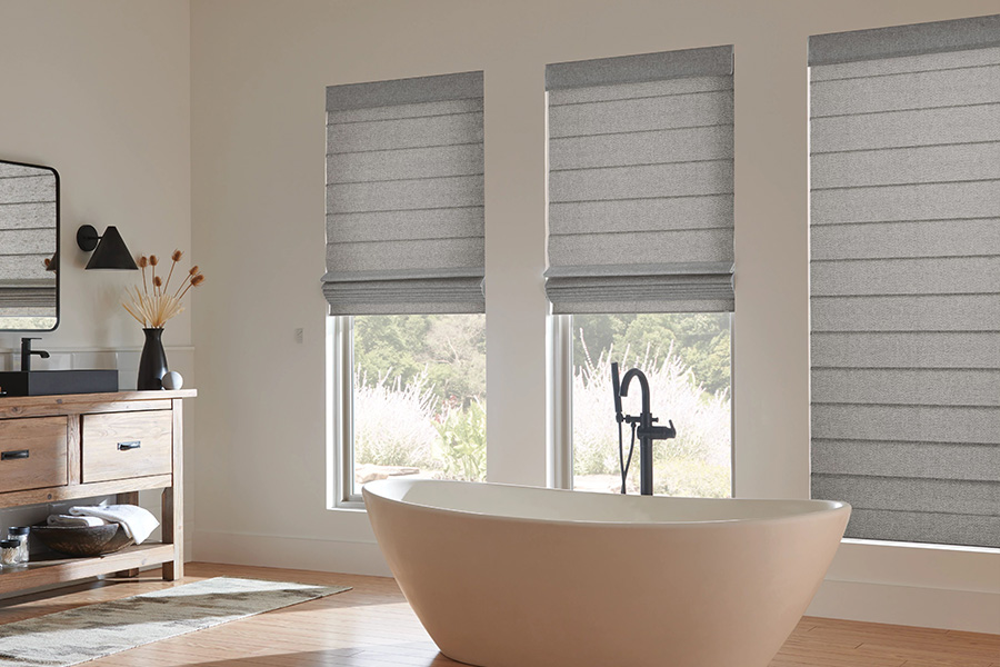 The soft pleats of Roman shades add a touch of luxury to any room. Gray Roman shades on bathroom windows