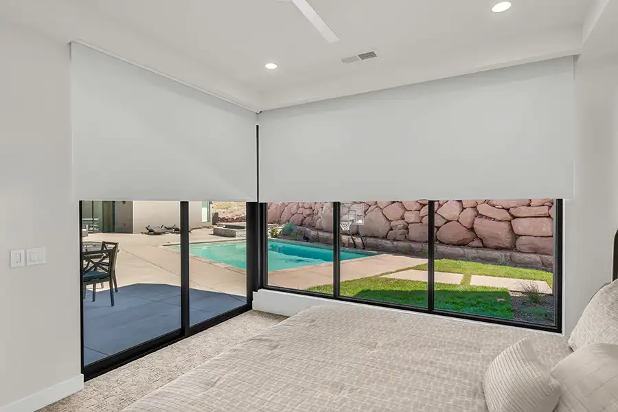 Large white shades on walls of windows in a bedroom overlooking a pool