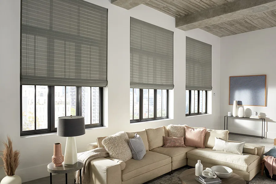 Gray woven shades pulled halfway down three windows in a modern living room decorated with neutral colors